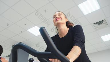 微笑女人培训室内自行车骑自行车类健身房快乐女人旋转自行车健身培训低角视图健身女人培训静态自行车